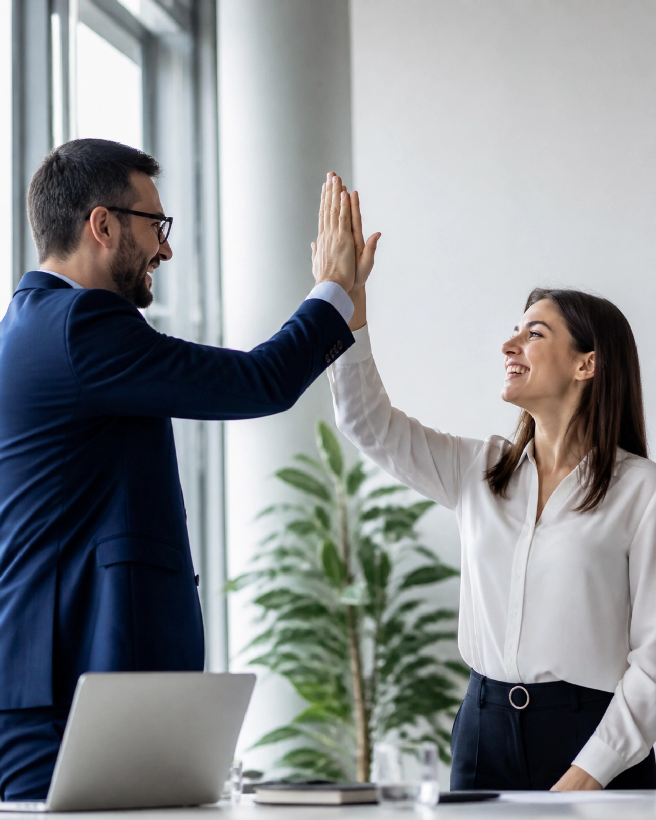 Colleagues high-fiving in a modern office, celebrating a closed deal.
