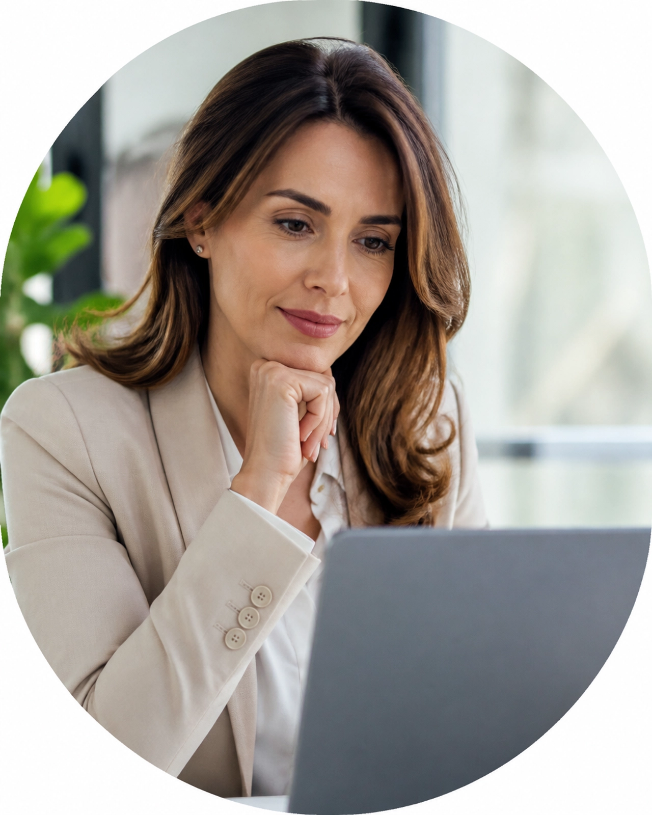 A professional woman looking thoughtfully at a laptop screen in a sunlit workspace